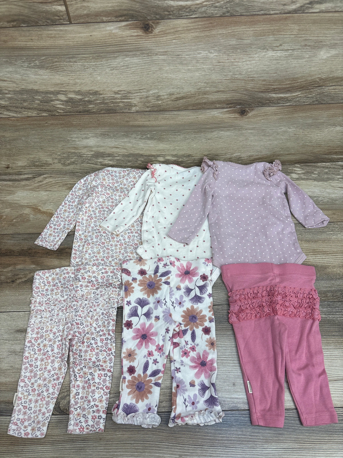 Top-down view of Huggies 6pc Bodysuit and Ruffle Pants Set showing six floral and dotted pieces on a wood floor