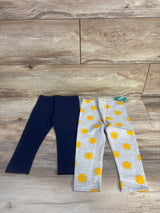 Flat lay of 2-pack toddler leggings, one solid navy and one light grey with yellow smiling sun print, size 18 months on wood floor background