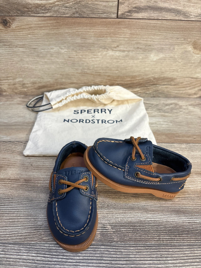 Navy blue Sperry kids boat shoes with brown laces and stitching, drawstring bag in background