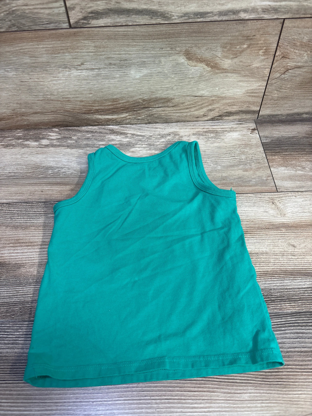 Flat lay of green Cat and Jack toddler tank top (3T) showing sleeveless design and hem stitching on wood floor background