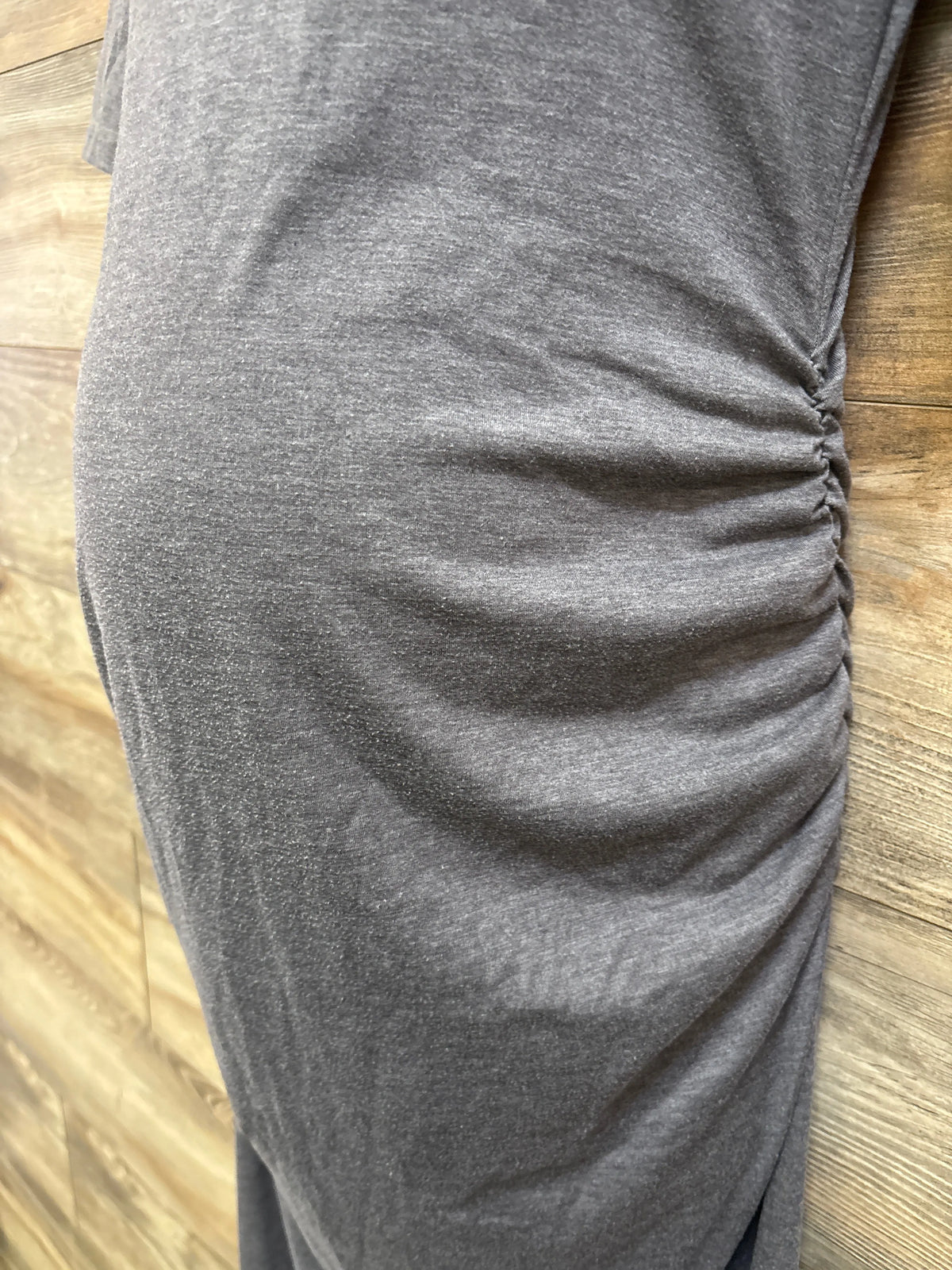 Close-up of gray Motherhood Maternity bodycon dress showcasing ruched side detailing on a wood floor