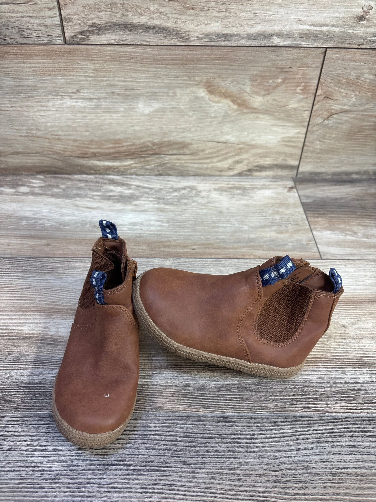 Front view of Cat & Jack brown toddler zipper ankle boots showing elastic side panel and blue pull tabs on wood floor
