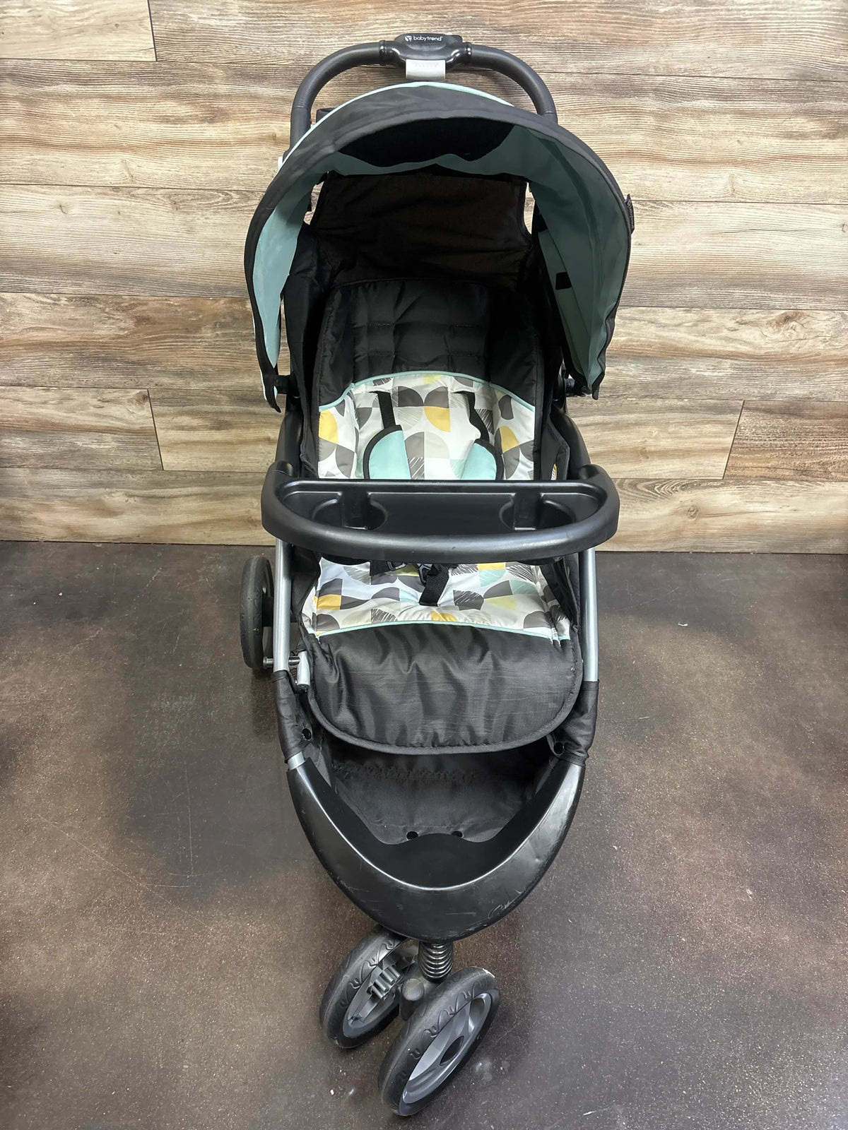 Front view of Baby Trend EZ Ride stroller in Doodle Dots with canopy and child tray with cup holders on wood flooring