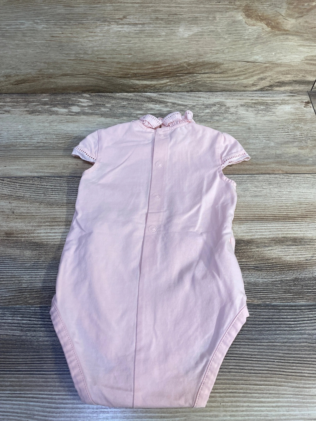 Top view of Mayoral pink ruffle-collar bodysuit showing back snaps and eyelet-trim sleeves on wood surface
