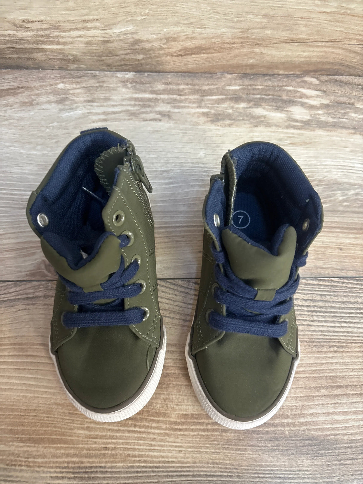 Pair of green toddler high-top sneakers with navy laces on wood floor