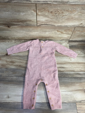 Soft pink fuzzy baby onesie with long sleeves and wooden buttons on gray wood floor