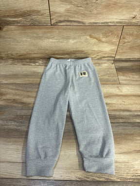 Flat lay of grey ribbed toddler pants showcasing elastic waistband and cuffed ankles on wood floor background