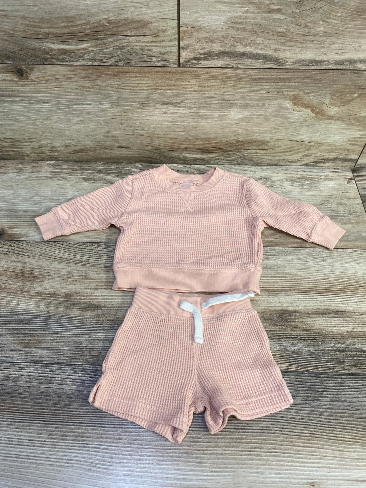 Flat lay of newborn pink thermal 2-piece set showing waffle texture, long-sleeve top and drawstring shorts on wood background