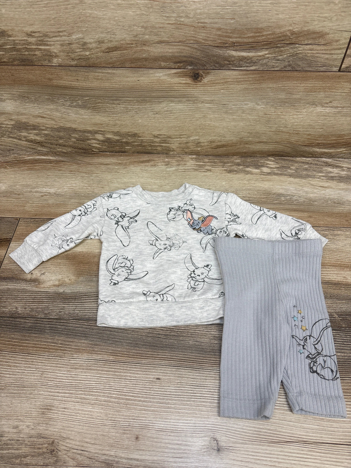 Top-down view of Disney Baby Dumbo sweatshirt and leggings set showcasing grey prints and ribbed leggings on a wood background