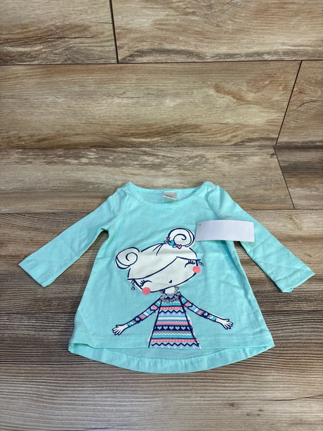 Mint green long sleeve toddler shirt with girl cartoon graphic, laid on wood floor