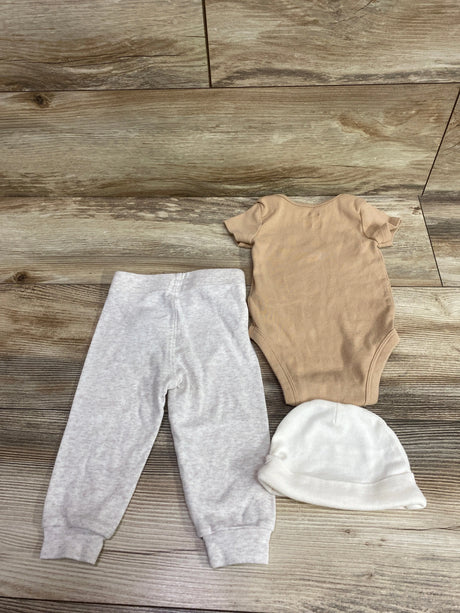 Nike 3-piece baby set featuring a tan bodysuit, grey pants, and a white hat on a wood floor.