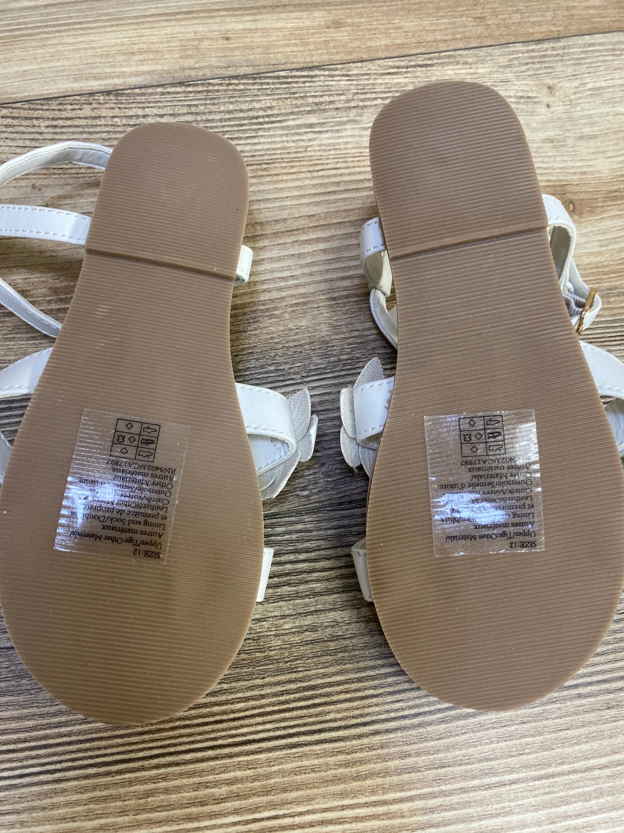 Janie & Jack toddler flower sandals, bottom view showing clean brown ribbed soles and size stickers on wood background