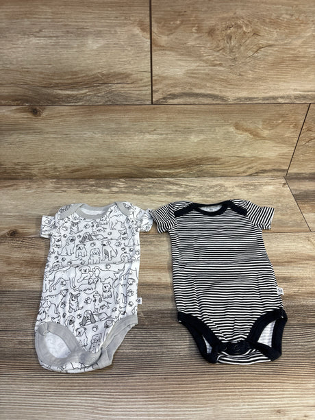 Flat lay of Honest Baby 2-pack bodysuits showing a white dog-print bodysuit with gray trim and a black-and-white striped bodysuit on wood background