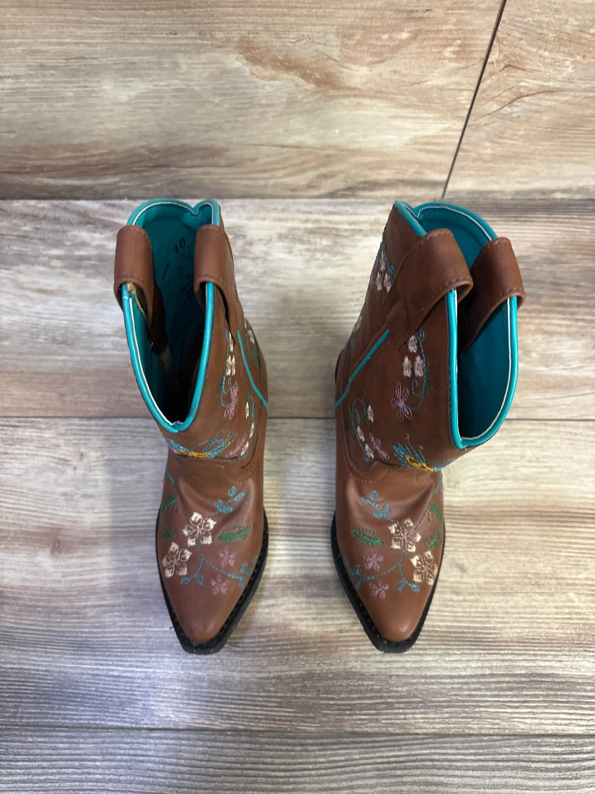 Top-down view of Shyanne brown floral-embroidered western boots showing turquoise lining and pointed toes on wood floor