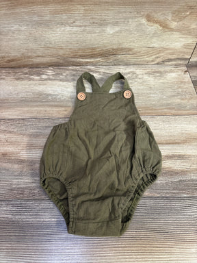 Top-down view of green linen baby romper showcasing crossed straps with wooden button closures and elasticized leg openings on wood plank background