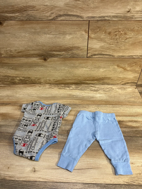 Flat lay of Champion gray printed short-sleeve bodysuit and light blue pants, size 3M, showing front view, snap closures, and elastic waistband on wood background