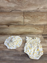 Top-down view of white 0-3M floral smocked bubble romper and matching sun hat showcasing ruffled smocking, snap crotch and yellow flower print on wood background