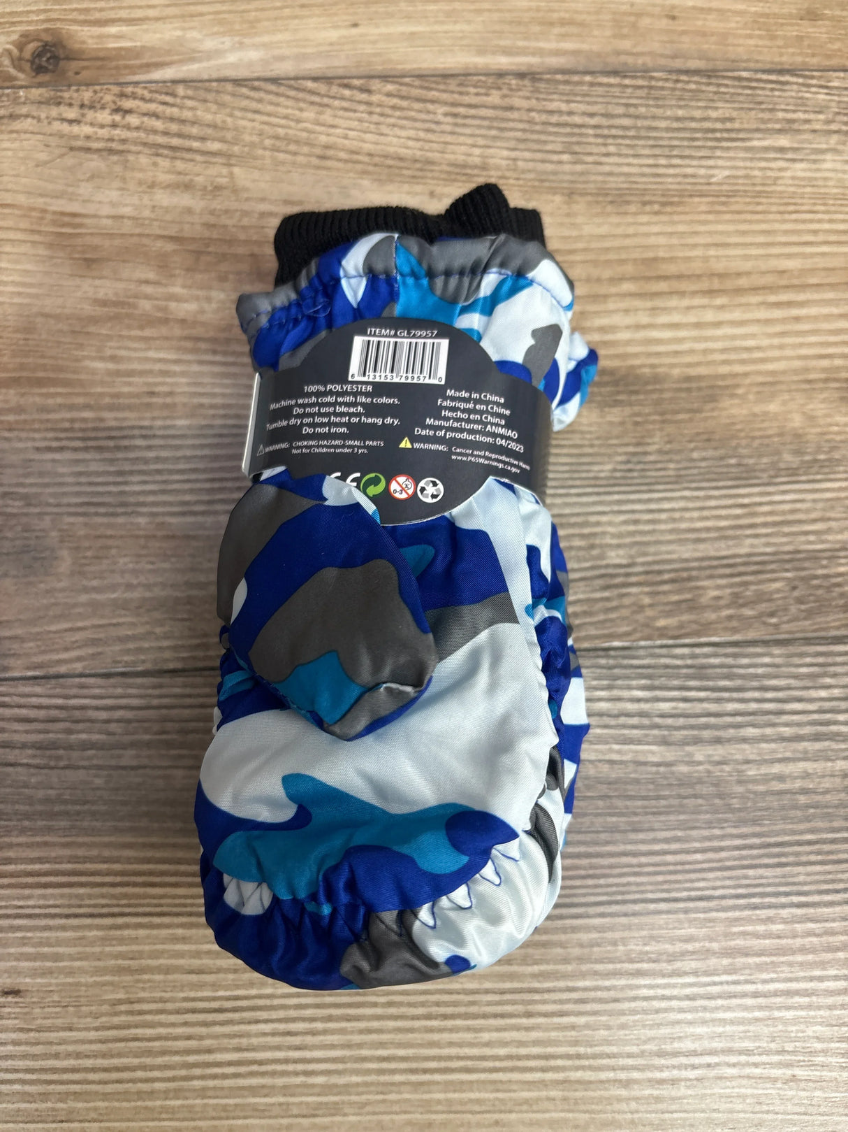 Blue and gray camouflage toddler mittens with black cuffs on wooden surface, children's winter gloves