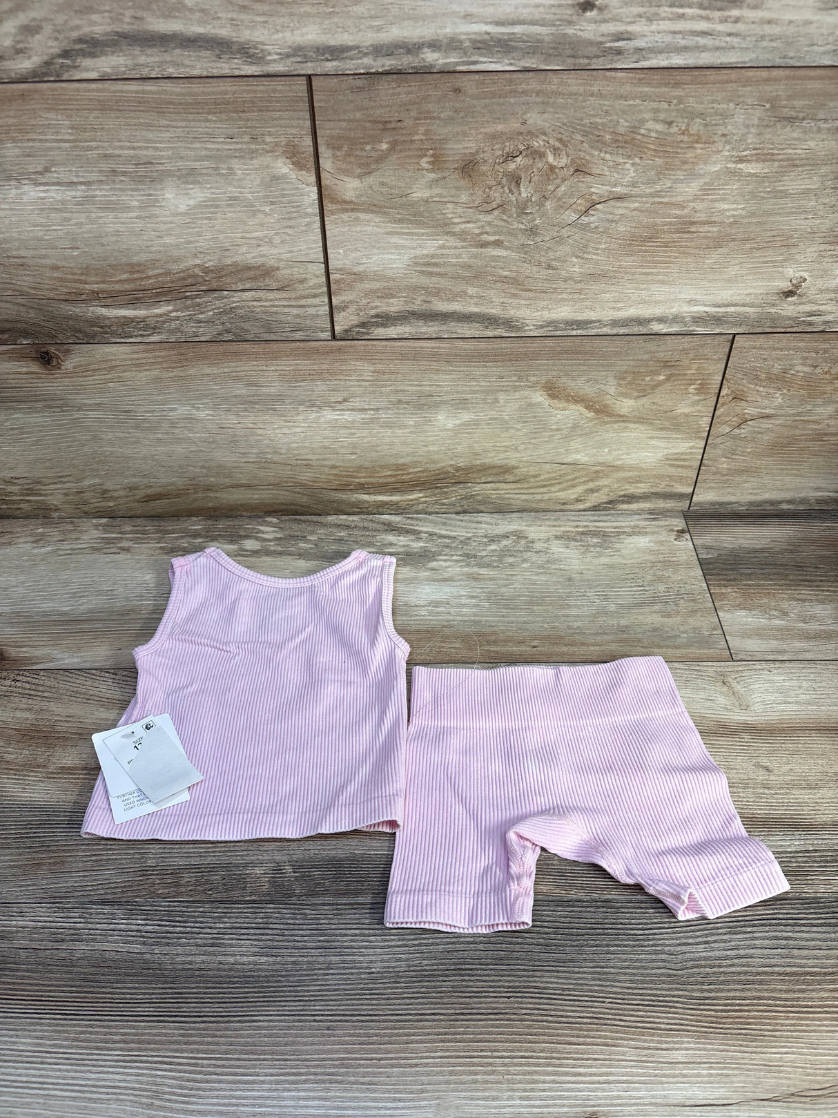 Flat lay of pink ribbed tank and bike shorts set (12M) showing ribbed texture on wood background