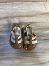 Top-down view of Cat & Jack soft-sole baby sandals showing tan faux-leather and white mesh straps on wood-plank background