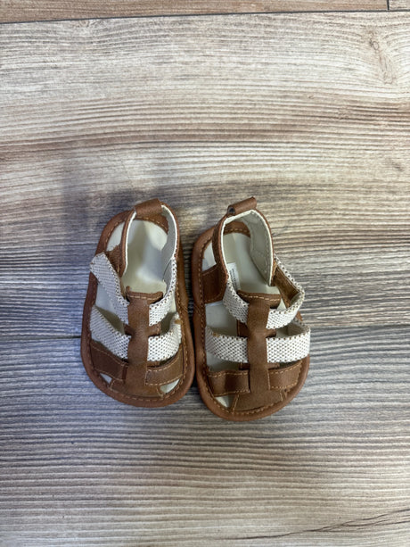 Top-down view of Cat & Jack soft-sole baby sandals showing tan faux-leather and white mesh straps on wood-plank background