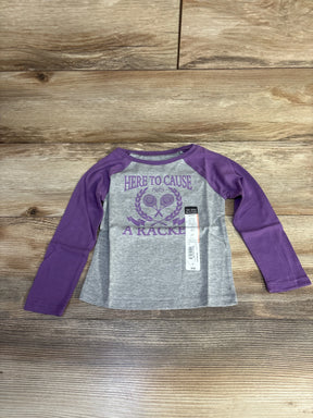 Flat lay of new Okie Dokie grey raglan tee with purple sleeves and Here To Cause A Racket tennis graphic with hangtag on wood plank floor
