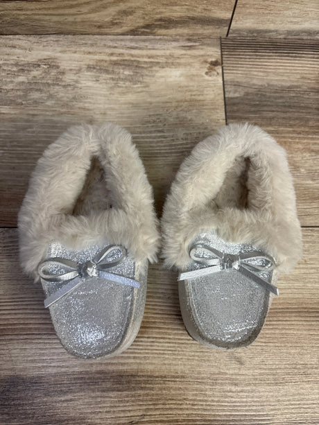 Pair of silver glitter toddler slippers with plush cream fur lining and silver bows on wooden floor