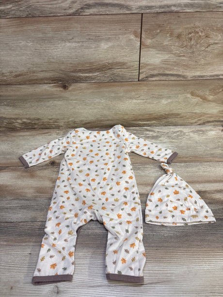 Top view of beige two piece baby coverall and hat set showcasing autumn leaf print and dark trim with wood grain background