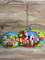 Front view of Cocomelon MacDonald Farm learning book showing cow and farmer, buttons and ladybug handle on wood floor