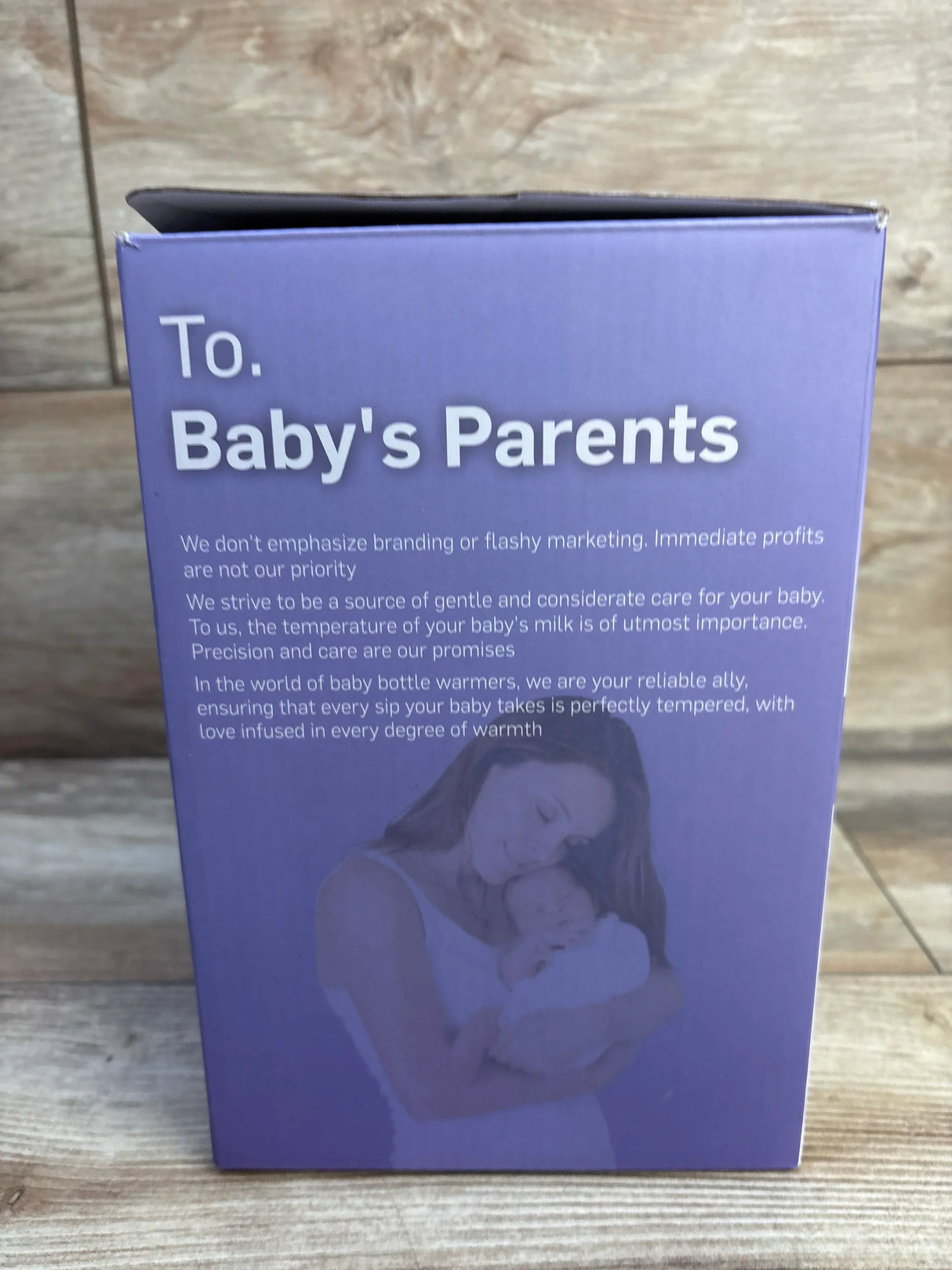 Front of Kumikimi bottle warmer box showing headline To. Baby's Parents and photo of mom and baby on wood background