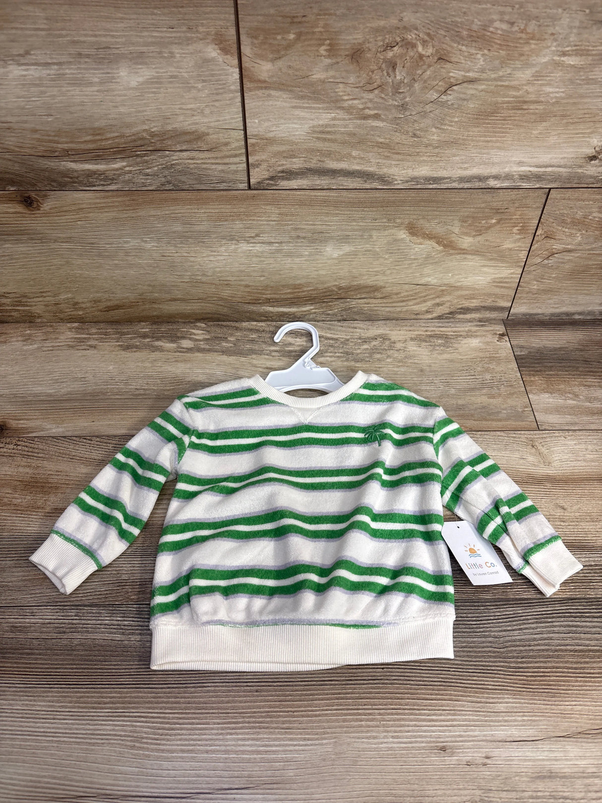 Kids white and green striped long sleeve sweater with palm tree embroidery, on plastic hanger over wooden background