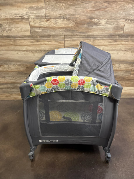 Front view of Baby Trend Lil Snooze playard with gray frame, Funfetti circle trim, mesh sides, canopy and wheels