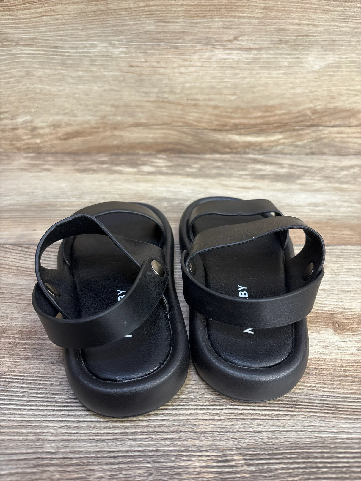 Top-down view of MGBABY black foam toddler sandals showcasing two straps and cushioned sole on wood background