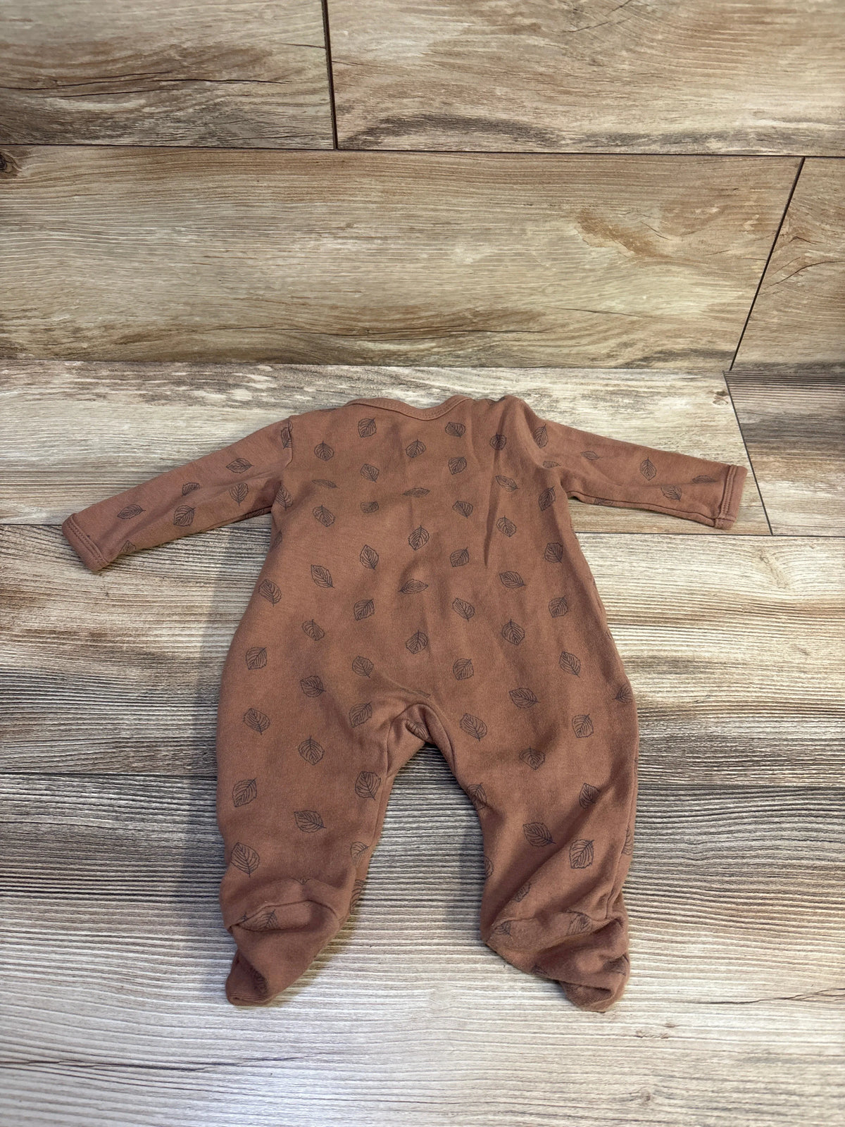 Front view of brown side-snap sleeper in size 3 months showcasing long sleeves with a leaf pattern and footed legs on a wood-look floor