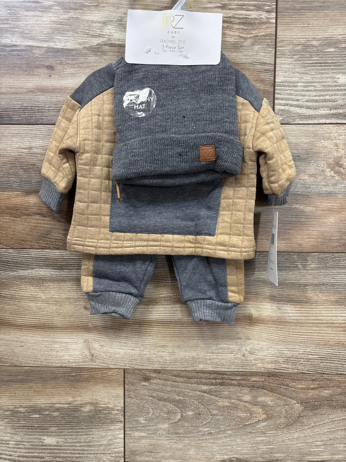 Rachel Zoe baby 3-piece set with grey and tan quilted sweatshirt, pants, and knit hat on wood background