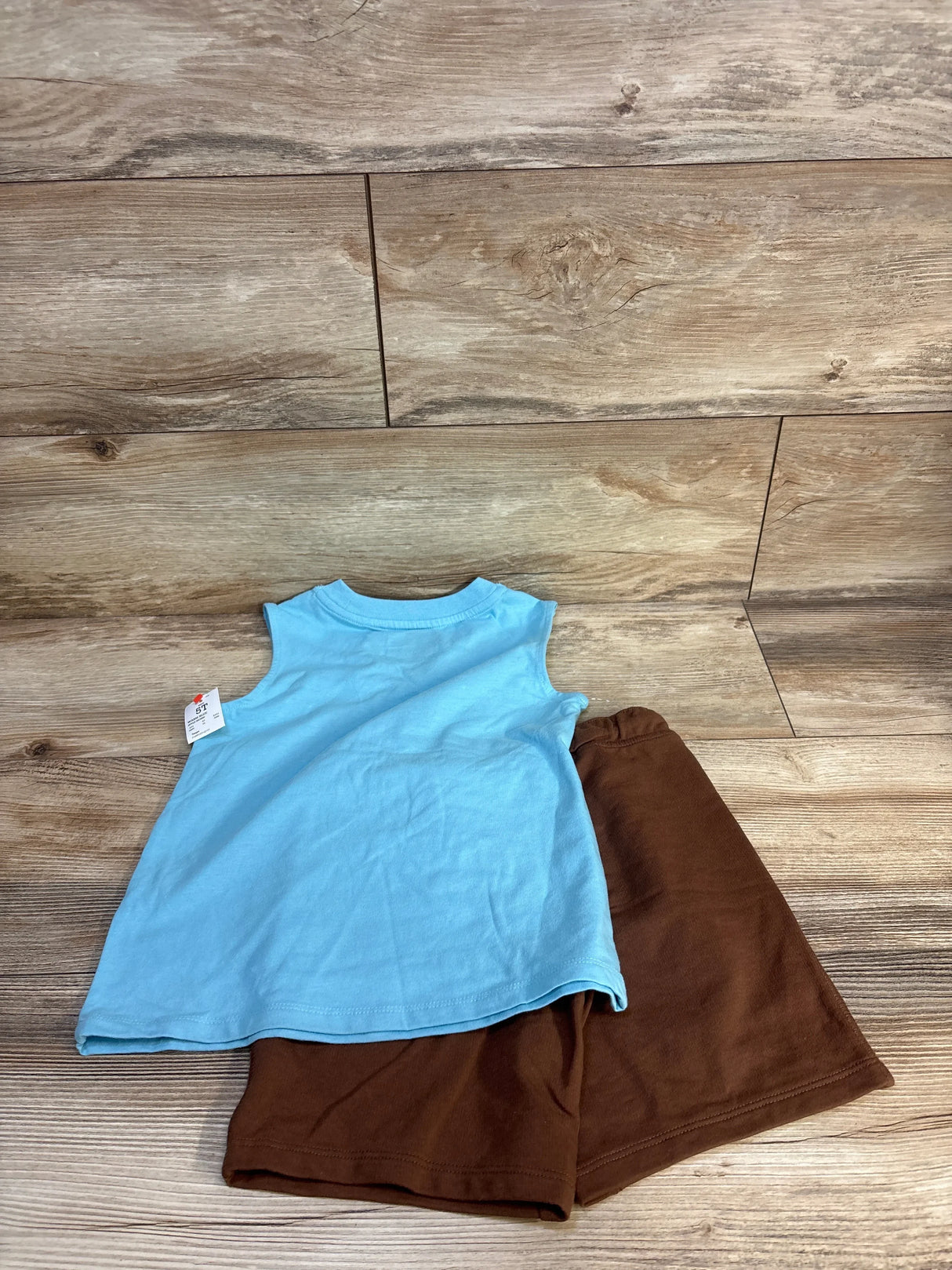 Blue sleeveless toddler dress with brown shorts on wood background, used kids clothes
