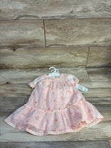 Flat-lay of pink floral baby dress (12M) showcasing ruffled hem and puff sleeves with wood plank background