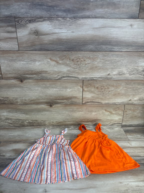 Top-down view of two 6-9M girls' sleeveless dresses, one solid orange and one multicolor striped on light wood floor