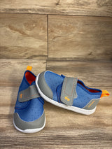 Three-quarter view of Ryder FlexiRun toddler water shoe in blue showing gray toe and strap, orange tab on wood background