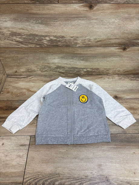 Front view of gray First Impressions full-zip jacket with light-gray sleeves and yellow smiley patch on wood background