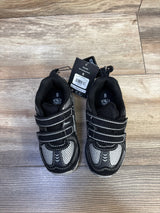 Top-down view of Athletic Works toddler two-strap black sneakers showing two Velcro straps, gray mesh panels, and attached hang tag on wood floor