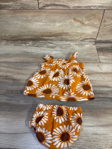 Flat lay of baby 2-piece sunflower top and bloomer set with elastic straps and waistband, white sunflower print on golden orange, on wood floor