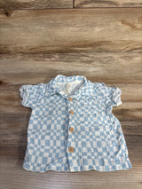 Flat-lay of baby gauze checkered shirt in light blue and white with wooden buttons and puff sleeves on wood background