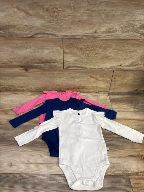 Overhead view of Honest Baby three piece bodysuit set showcasing white, navy, and pink long sleeve bodysuits with ruffled shoulders on a wood floor