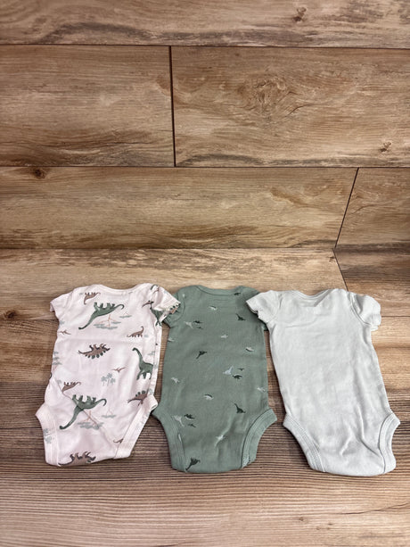 Top view of three Just One You newborn bodysuits with dinosaur prints and solid white design on a wood background