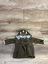 Flat lay of green dinosaur baby bath robe showing hood spikes, printed leaf lining, and tied waist belt on light wood background