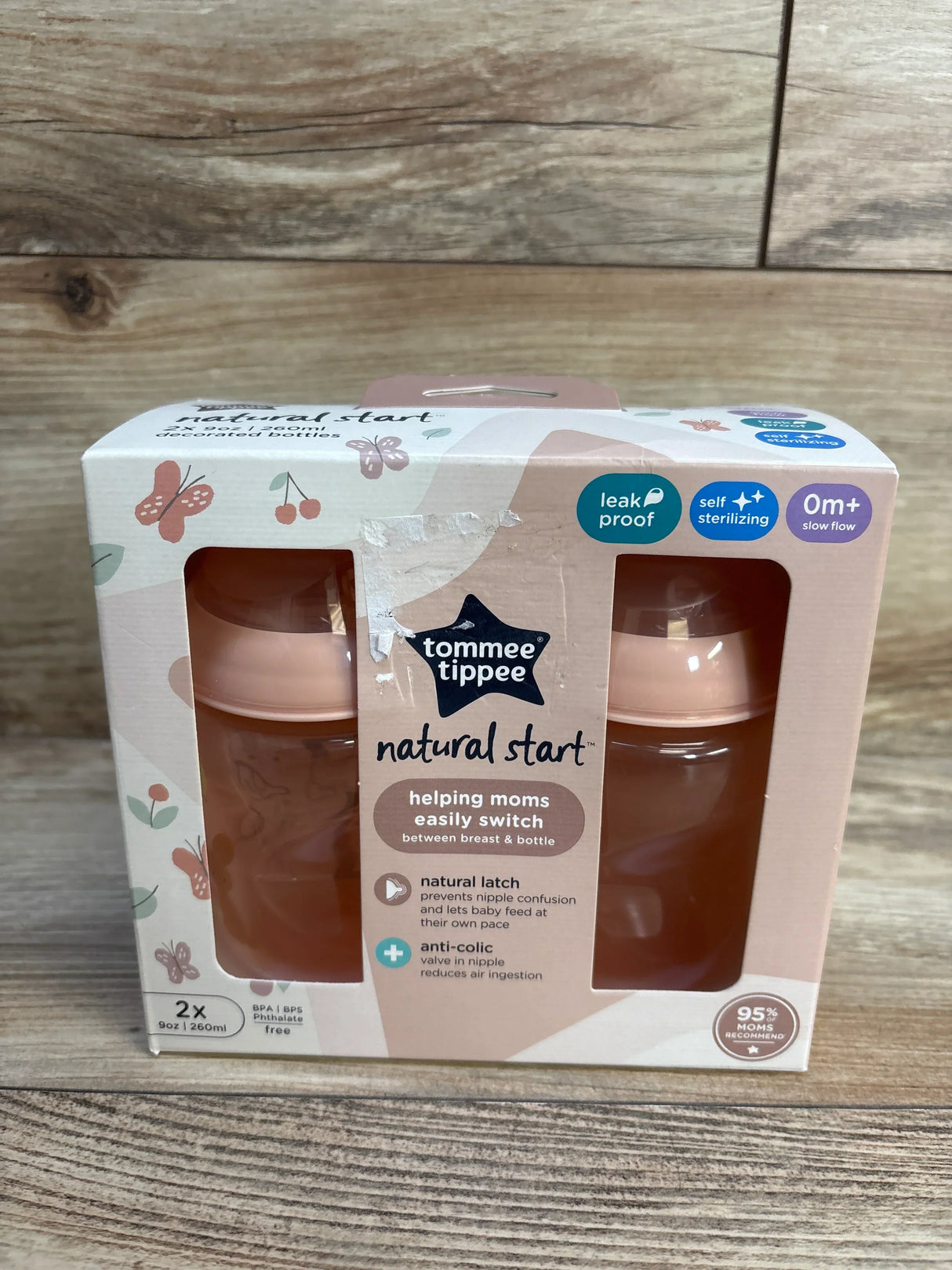 Front of Tommee Tippee Natural Start 9oz 2-pack showing pink bottles in box with natural start headline on wood background
