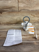 Rear view of white VTech Myla monkey soother with gray hanging loop, USB cable, and manual on wood background