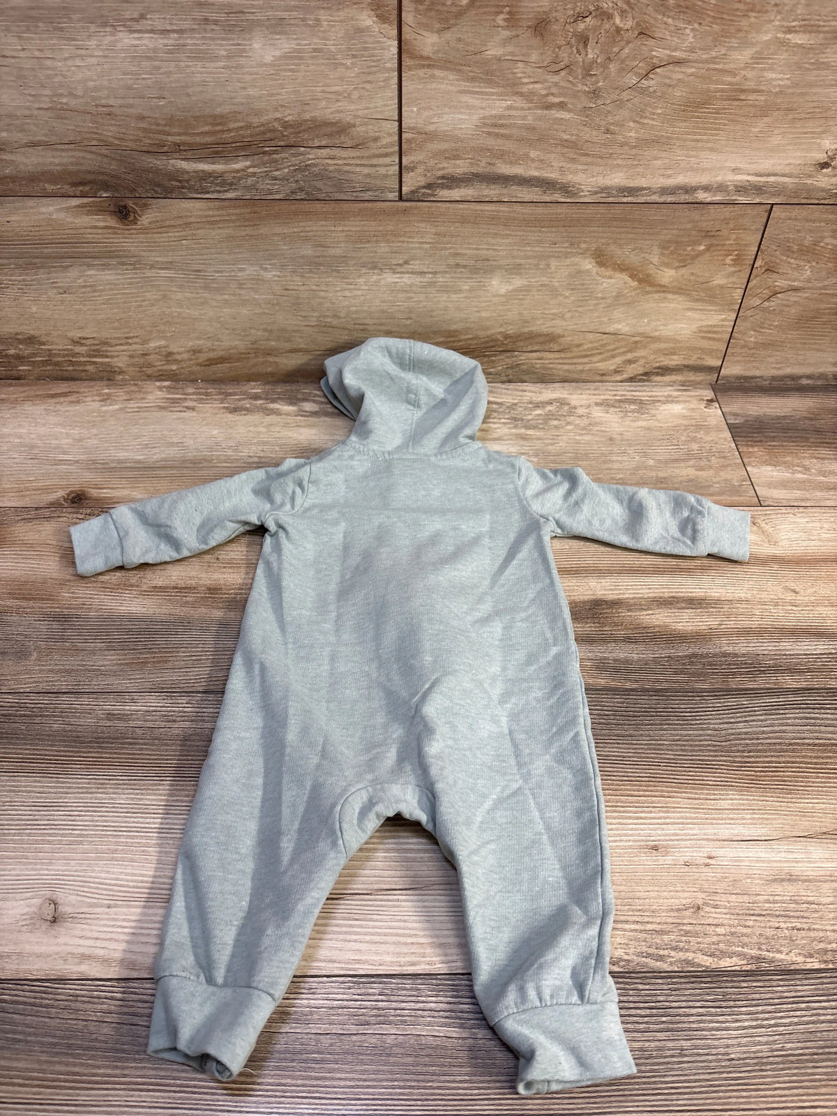 Front view of Nike sage hooded coverall showcasing long sleeves and an attached hood on a wood-look background