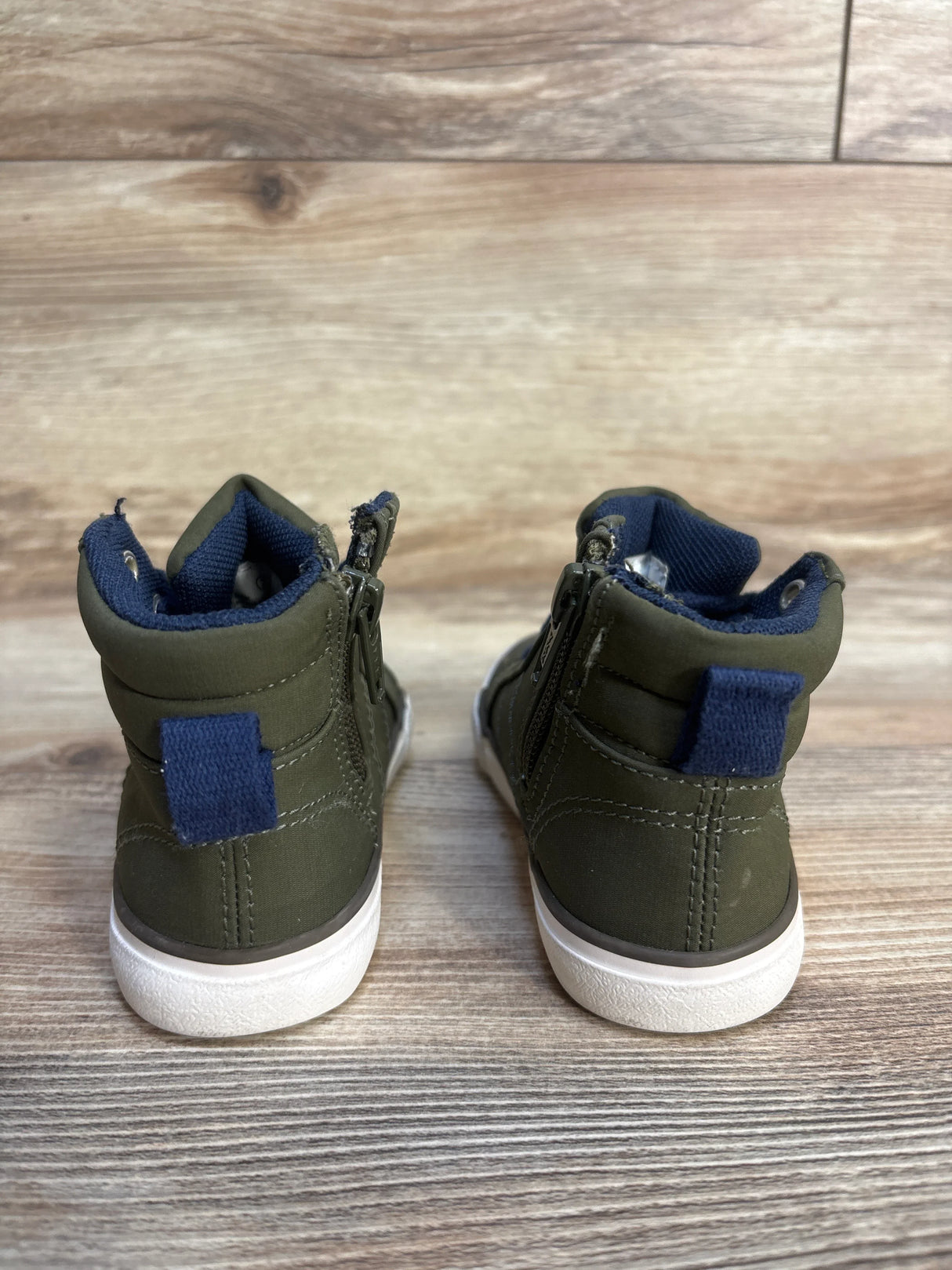 Back view of olive green toddler high top sneakers with white soles on wood floor